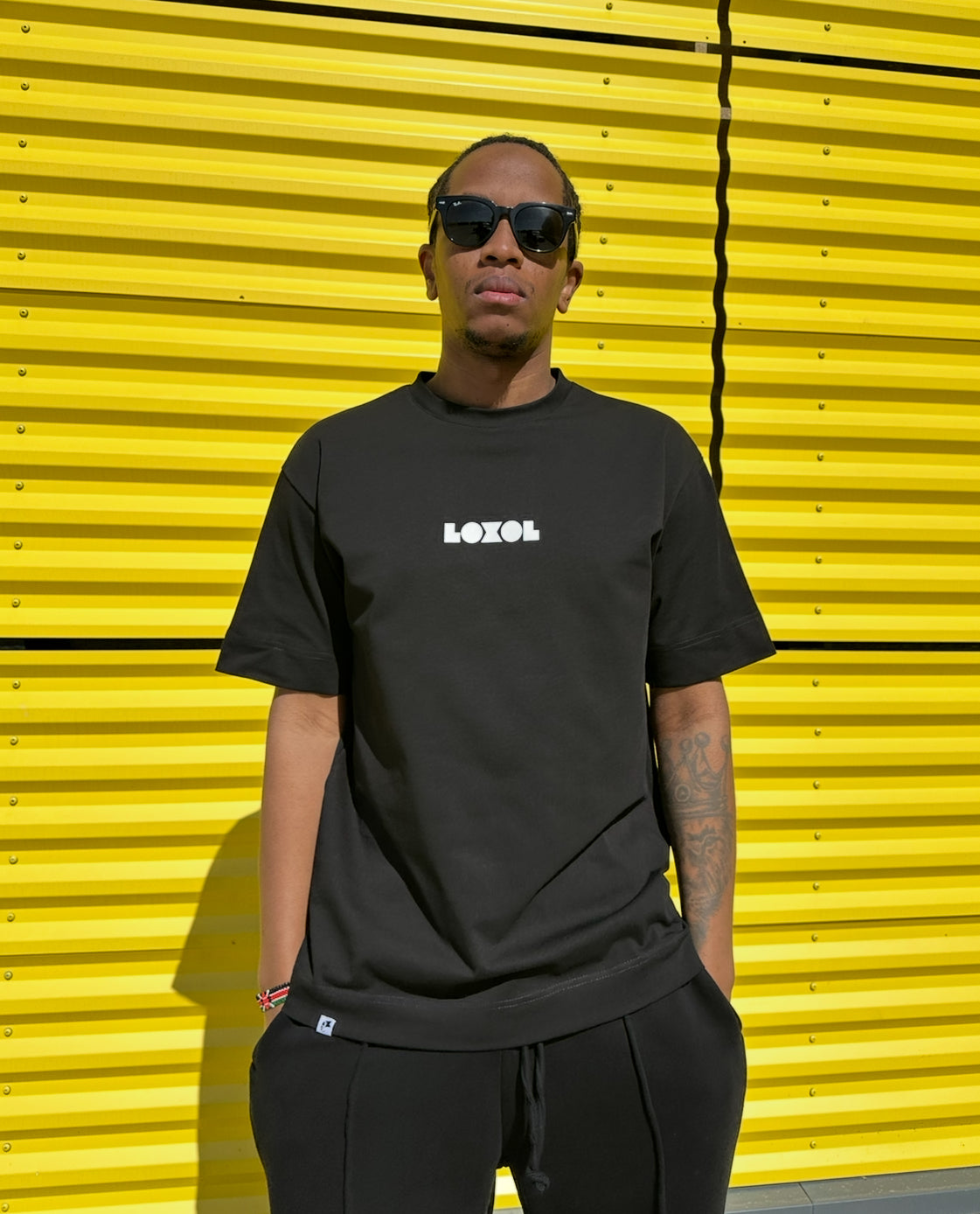 A person wearing a white everyday T-shirt with a brand logo, standing in front of a yellow background.